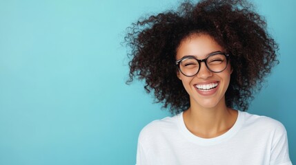 A happy woman with glasses and curly hair exudes joy while wearing a white t-shirt. The vibrant blue background enhances her radiant smile