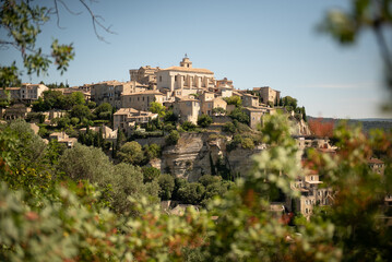 Distant view of the town of Gordes up in a hill under a blue sky in summer, in the Vaucluse département in the Provence-Alpes-Côte d'Azur region in southeastern France.