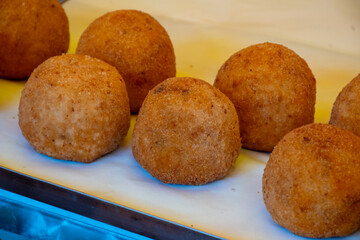 Sicilian street food arancini, deep fried rice croquettes with different fillings on market