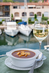 Homemade tasty fish or bisque soup with croutons served with glass of cold white wine and view on yacht boats and houses of Port Grimaud, French Riviera, France. Food of Provence