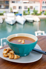 Homemade tasty fish or bisque soup with croutons and view on yacht boats and houses of Port Grimaud, French Riviera, France. Food of Provence