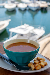 Homemade tasty fish or bisque soup with croutons and view on yacht boats and houses of Port Grimaud, French Riviera, France. Food of Provence