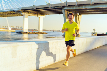 Jogger in Bright Yellow Shirt Runs Along Waterfront Trail Under Sunny Sky in Modern Cityscape...
