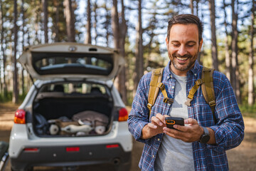 adult man camper use mobile phone in front car in the forest