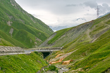 Naklejka premium A winding road leads through a lush green valley, with mountains rising on either side.
