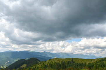 Landscape featuring mountain range covered dense forest under majestic sky above is filled with a mix of fluffy white clouds and darker, denser clouds, suggesting an approaching storm or rainfall