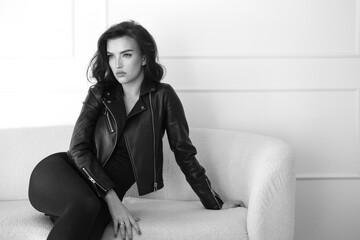 A stylish woman poses in a black leather jacket against a white background