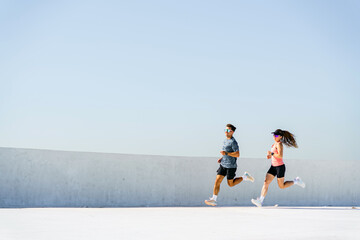 Two Fitness Enthusiasts Jogging Together Under a Clear Blue Sky in an Urban Environment During...