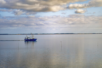 A fishing boat glides across calm waters under a cloudy sky in a serene lake during late afternoon