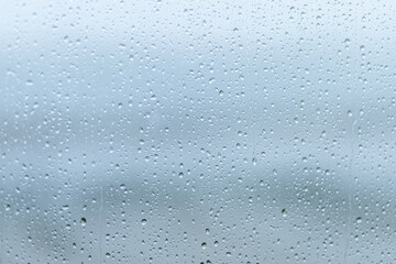 Raindrops cluster on a window pane during a grey overcast day, creating a serene atmosphere and blurring the outside view