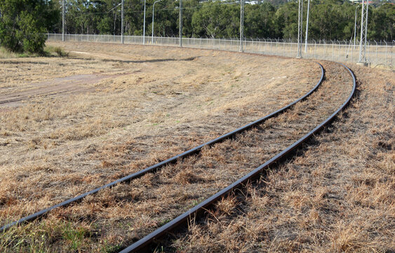 Railway tracks curving through a dry grassy landscape with trees in the background
