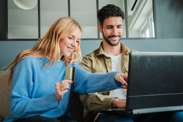 Couple using a laptop to make an online purchase with a credit card, smiling while shopping...
