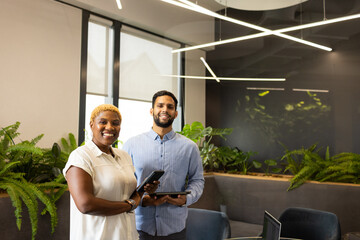 Smiling colleagues holding tablets in modern office with green plants, copy space