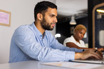 Obraz premium Working on laptop, african american man focusing on task while woman writing in background
