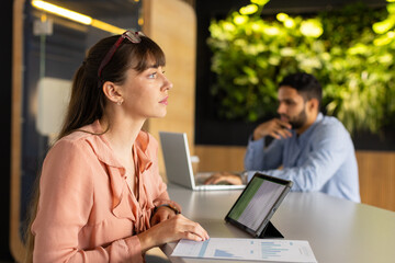 Working in office, woman using tablet and holding document with graphs