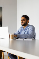 Naklejka premium Working on laptop, man smiling with coffee cup and notebook on table