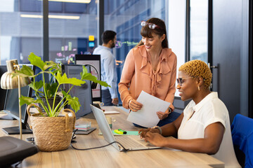 Collaborating at office, two women using laptop and documents discussing project