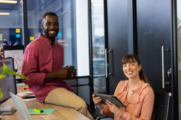 Collaborating on project, smiling colleagues in office using tablet and holding coffee