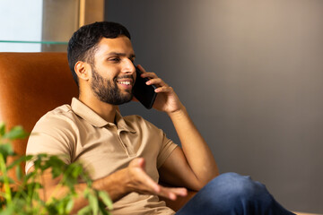 Talking on smartphone, man sitting on chair and smiling, enjoying conversation