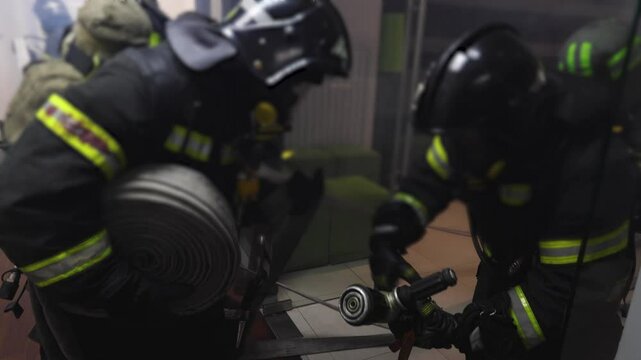 Group of firefighters in protective uniform during fire fighting operation inside the office building corridor, firemen brigade during fire drill, emergency and rescue service, exercise and training
