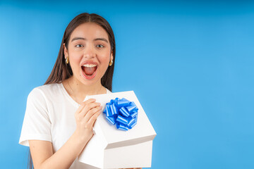 Excited woman holding a gift with blue ribbon on blue background