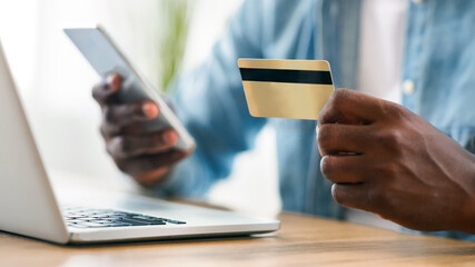 Online payment. Unrecognizable african american man using credit card and smartphone for paying bills in internet, closeup