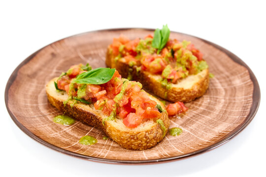 Traditional Italian appetizer,homemade bruscheta with tomatoes and basil served on brown plate, isolated on white background