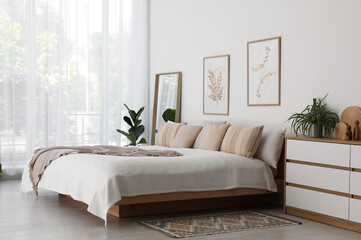 Large bed, houseplant and full-length mirror near window in room. Stylish bedroom interior