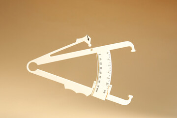 Plastic body fat caliper on beige background