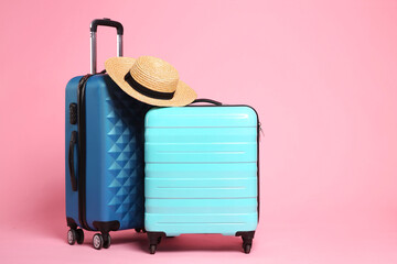 Two new color suitcases and wicker hat on pink background, space for text