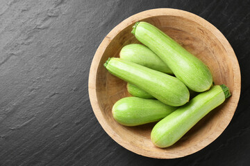 Fresh zucchinis in bowl on dark textured table, top view. Space for text