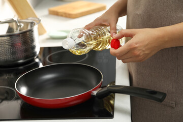 Woman with bottle of oil and frying pan in kitchen, closeup