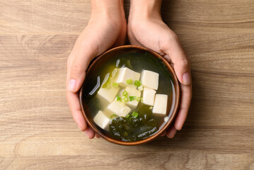 Miso soup with tofu, wakame seaweed and spring onion in bowl with hand, Traditional Japanese soup,...