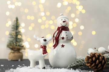 Funny snowman figure and decorative reindeer on table against blurred lights