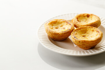 Stack of Portuguese sweet dessert egg tart or Pastel de Nata on white ceramic plate on white table. Copy space. Selective focus.