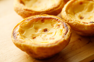 Stack of Portuguese sweet dessert egg tart or Pastel de Nata on wooden board on wooden table.  Selective focus.