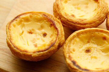 Stack of Portuguese sweet dessert egg tart or Pastel de Nata on wooden board on wooden table.  Selective focus.