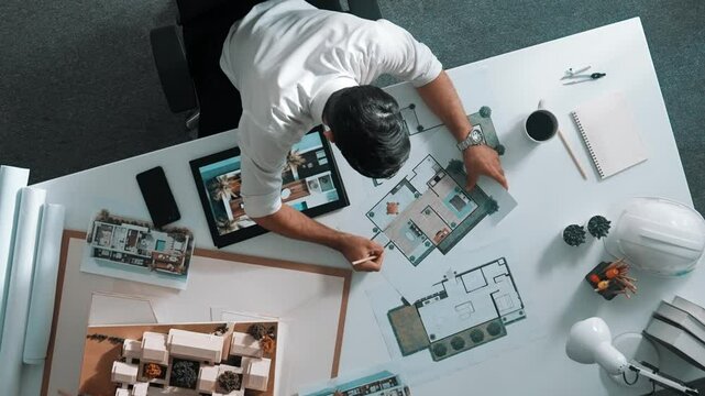 Top view of business man using tablet plan house design while sitting at meeting table with blueprint and equipment scatter around. Aerial view of civil engineer working at blueprint. Alimentation.