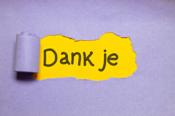 Dutch text “Dank je” (Thank you) written on yellow paper unveiled behind purple layer. Concept of gratitude.