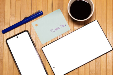 Mockup of a desk with a tablet and a smartphone with a blank screen next to a thank you note. A day at work.