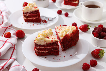 Pieces of red velvet cake on plates, berries and towel on white background