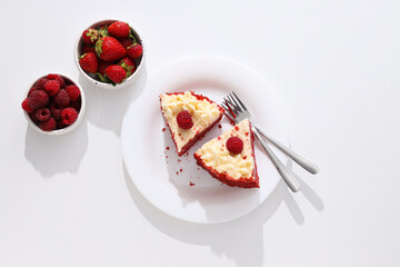 Pieces of red velvet cake on plate and berries on white background, top view