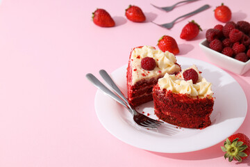 Pieces of red velvet cake on plate and berries on pink background, space for text