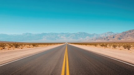 Fototapeta premium A long, straight road in the desert with mountains visible in the distance under a clear blue sky.