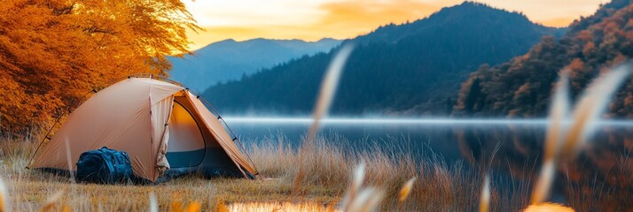 A peaceful lakeside campsite during autumn, featuring an orange tent nestled among golden grass