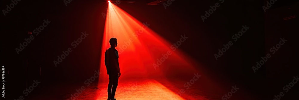 Poster in a dimly lit space, a shadowy figure is caught in a single, bright spotlight, creating an eerie at