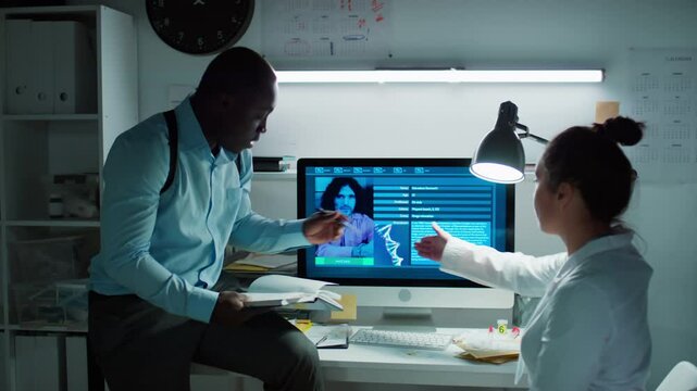 Female forensic scientist and male detective discussing profile of suspect displayed on computer monitor while working with criminal database during investigation in laboratory