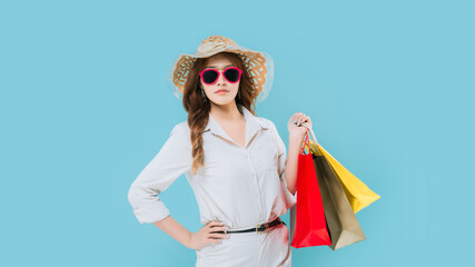 A woman is holding shopping bags and wearing a white shirt and a straw hat. She is posing for a photo