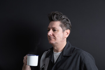 Man in his 50s with nice hair holding a cup of lightly steaming coffee. Dark background. Copy space. Concept of men, maturity and coffee