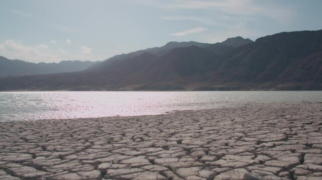 Cracked soil ground. Shore of Lake Bartogay. Hills against the backdrop of the lake. 4K video